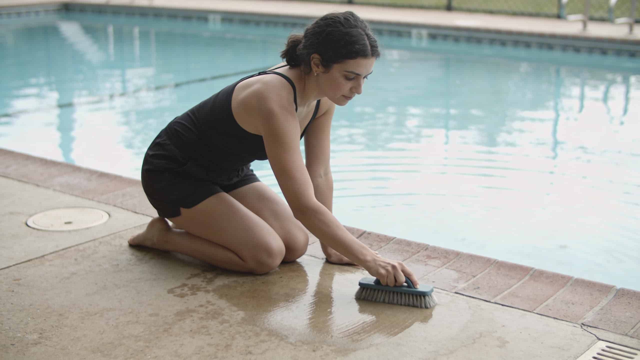 Femme agenouillee brossant piscine exterieure eau claire