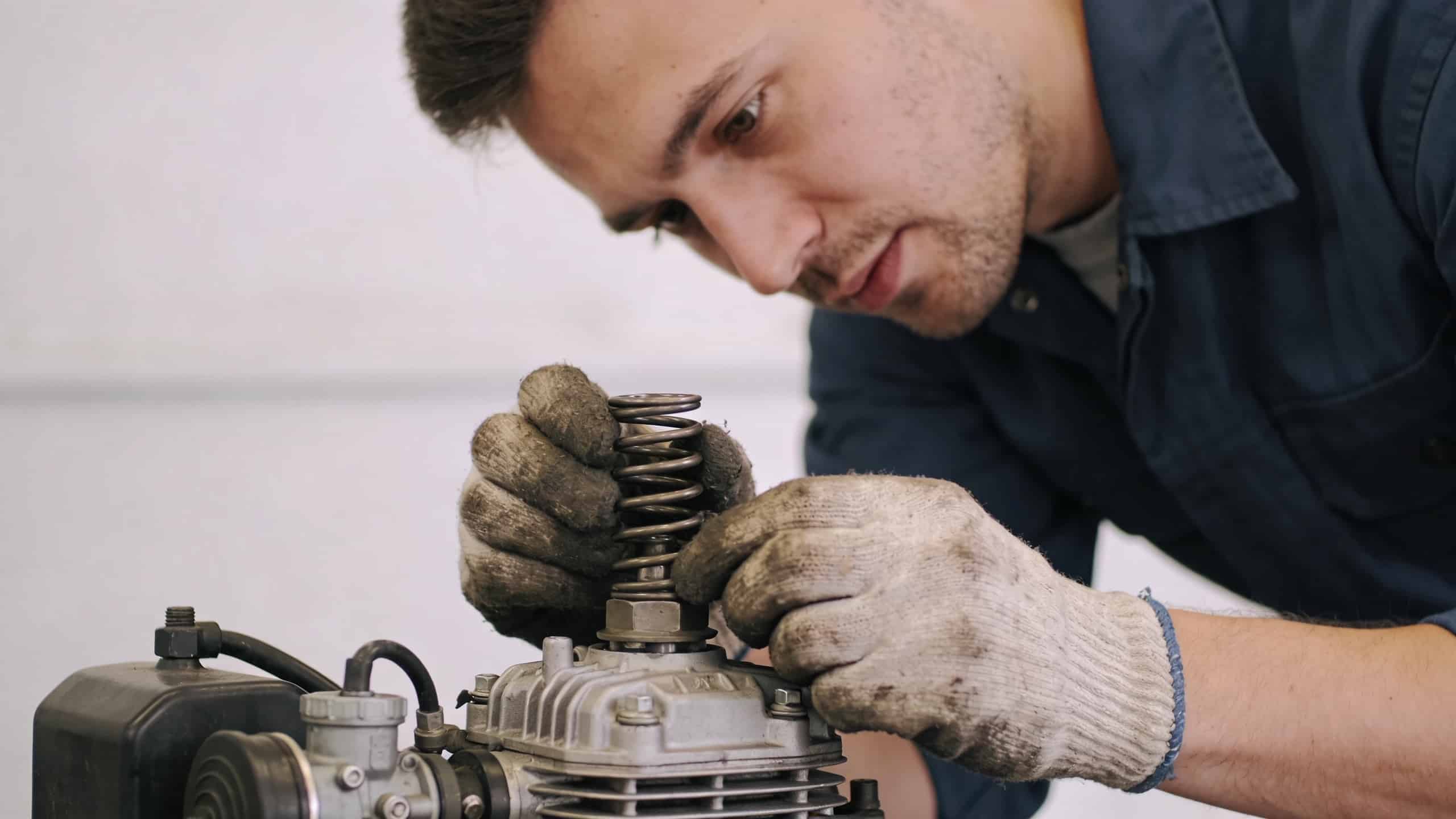 mecanicien penche fixant ressort regulateur sur petit moteur